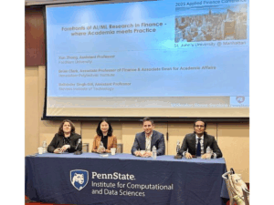 Four finance experts sit at a table with a blue Penn State Institute for Computational and Data Sciences tablecloth to present their research at a the Financial Management Association Applied Finance Conference in New York City.
