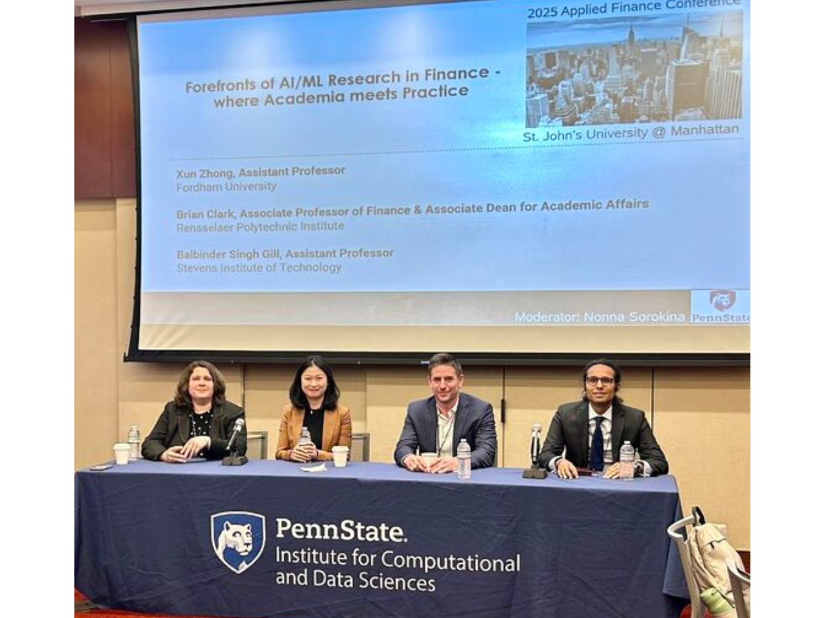 Four finance experts sit at a table with a blue Penn State Institute for Computational and Data Sciences tablecloth to present their research at a the Financial Management Association Applied Finance Conference in New York City.